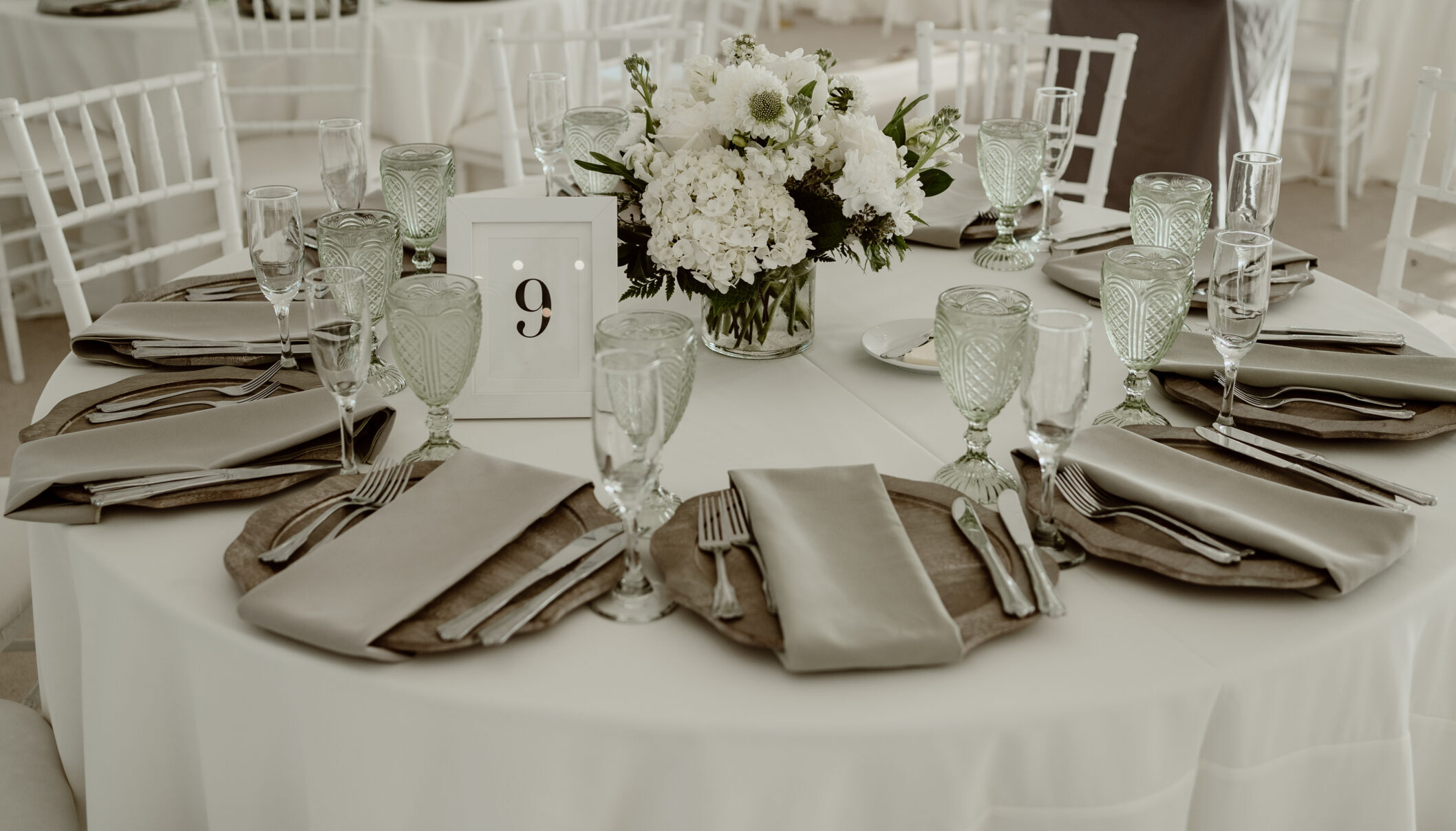 Gray napkins wrapped around gray and silver chargers on a wedding reception table.