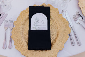 A black cloth napkin folded on a gold charger plate.