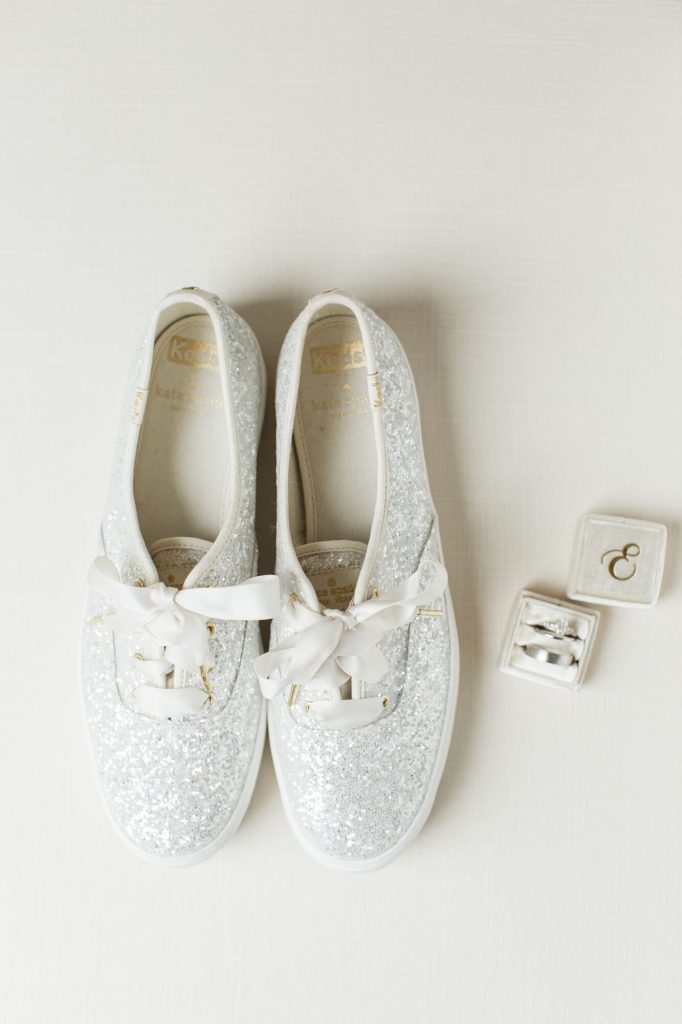 White glitter sneakers with ribbon laces beside a ring box.