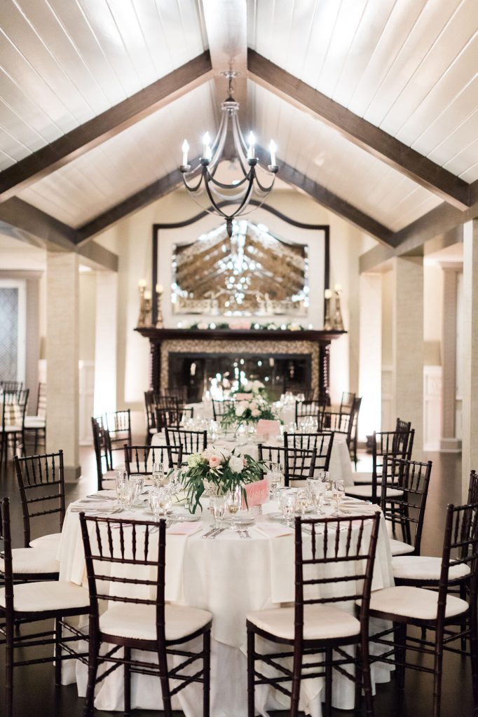 Reception hall with a vaulted beamed ceiling, chandelier and tables set with white flowers.