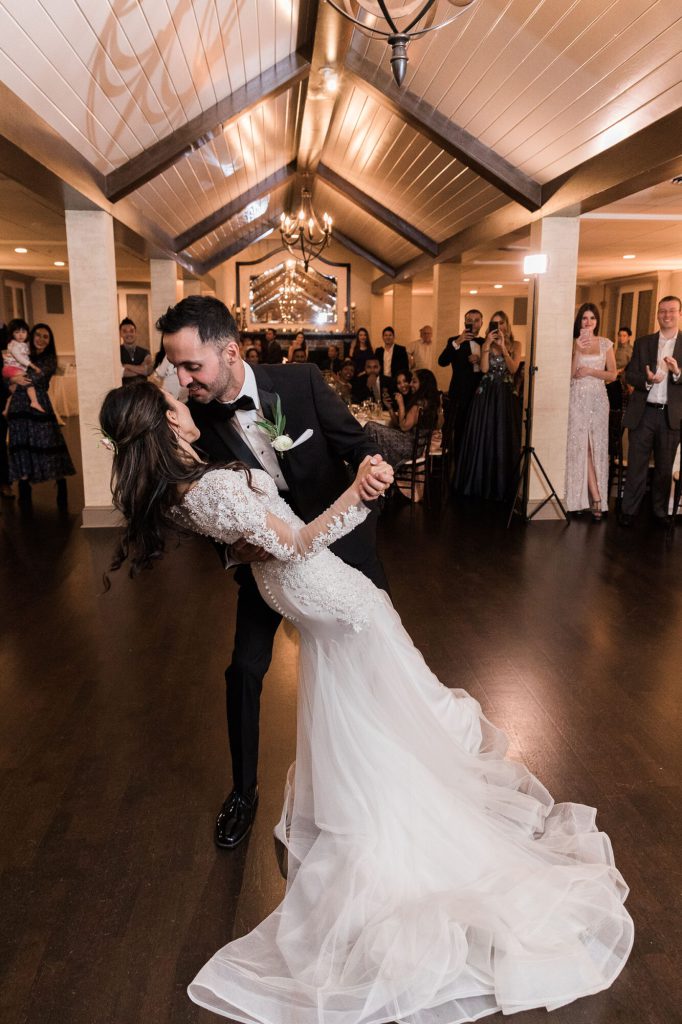 Groom dipping the bride during their first dance under a vaulted beamed ceiling.