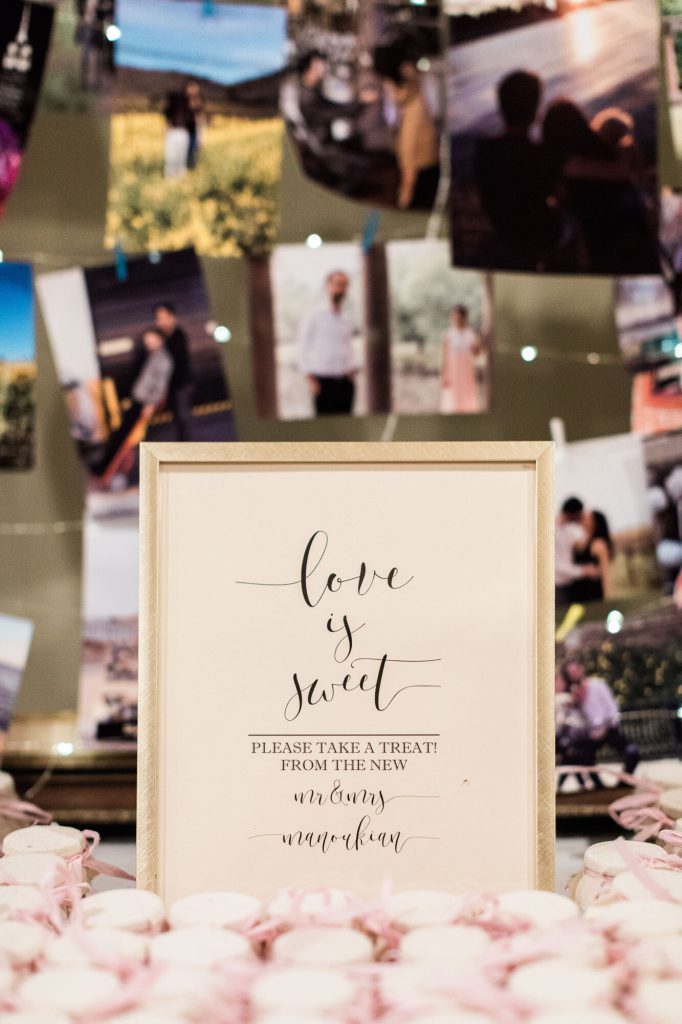 Dessert table with a sign reading Love is sweet, please take a treat, beside a photo wall.