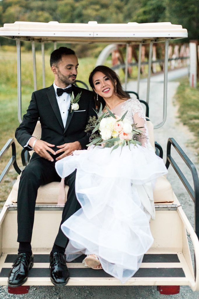 Bride and groom smiling side by side on the back of a golf cart.