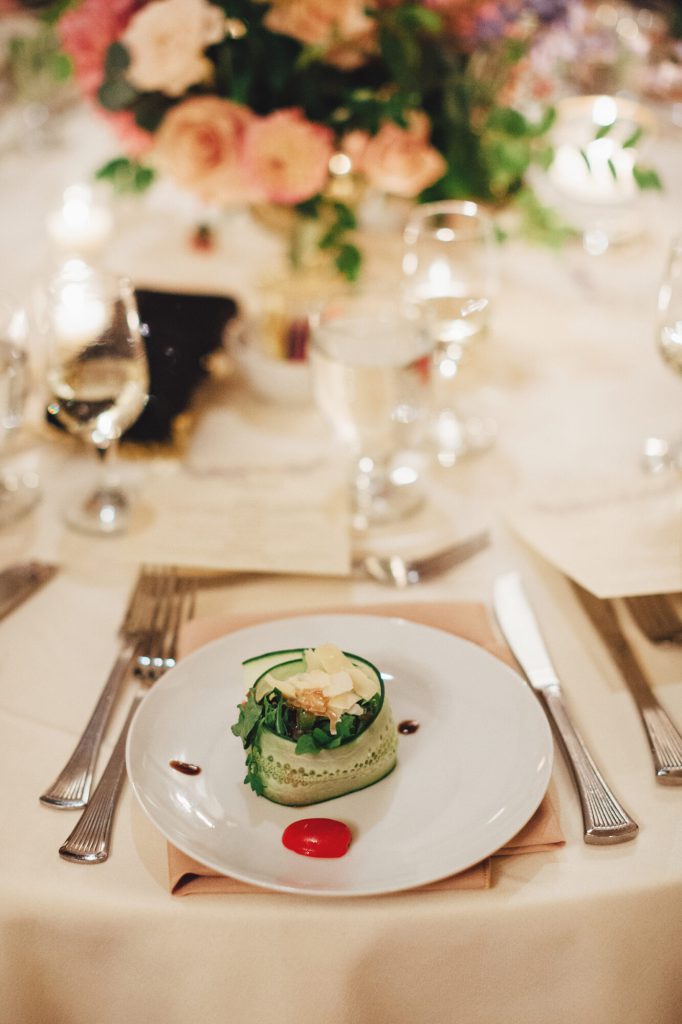 Reception place setting with a plated salad tower and a pink floral centerpiece.