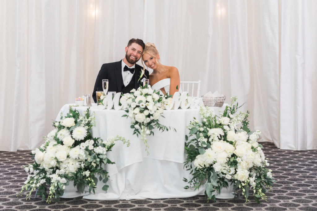 Bride and Groom Sitting at their Sweetheart Table with White Floral Arrangements