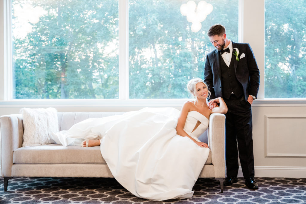 Bride Sitting on Couch with Groom Looking Down at Her