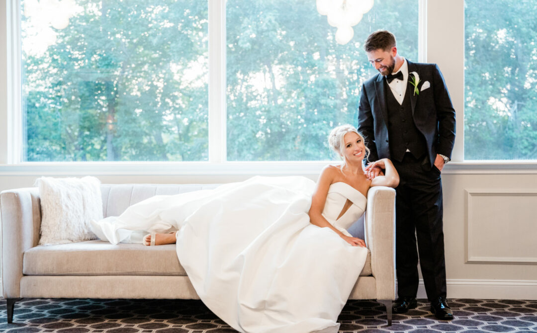 Bride Sitting on Couch with Groom Looking Down at Her
