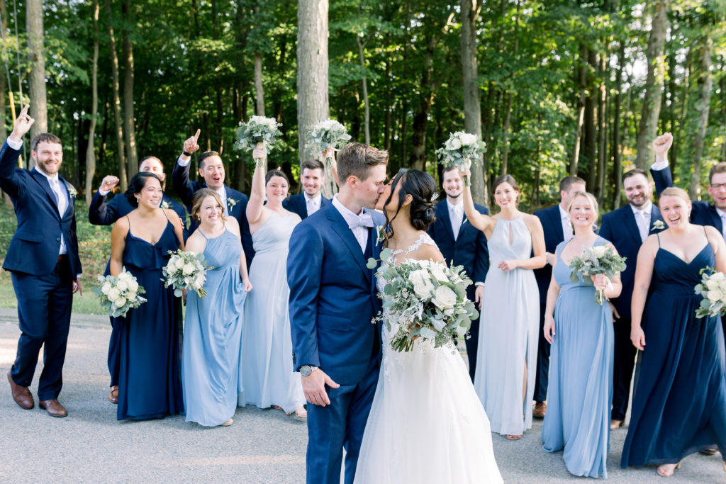 Wedding Party in Background with Couple Kissing and Smiling Blue Dresses and Suits