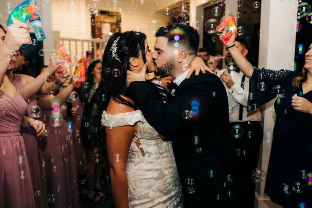 Bride and Groom Kissing in Bubbles During Their Wedding Send Off
