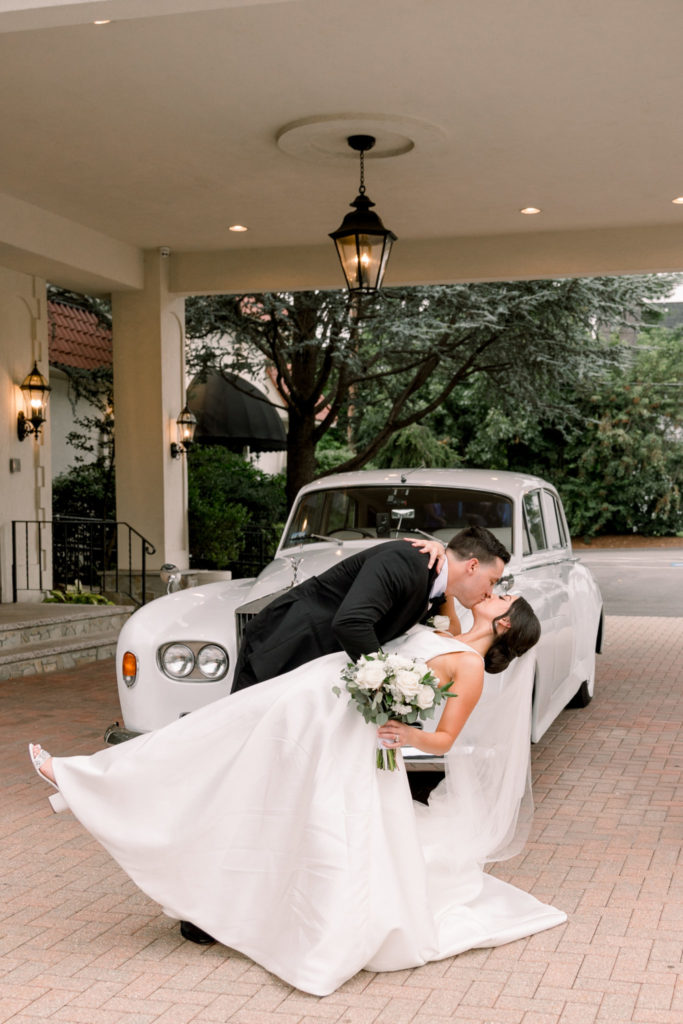 Wedding pose of groom leaning bride over for a kiss in front of a Rolls Royce