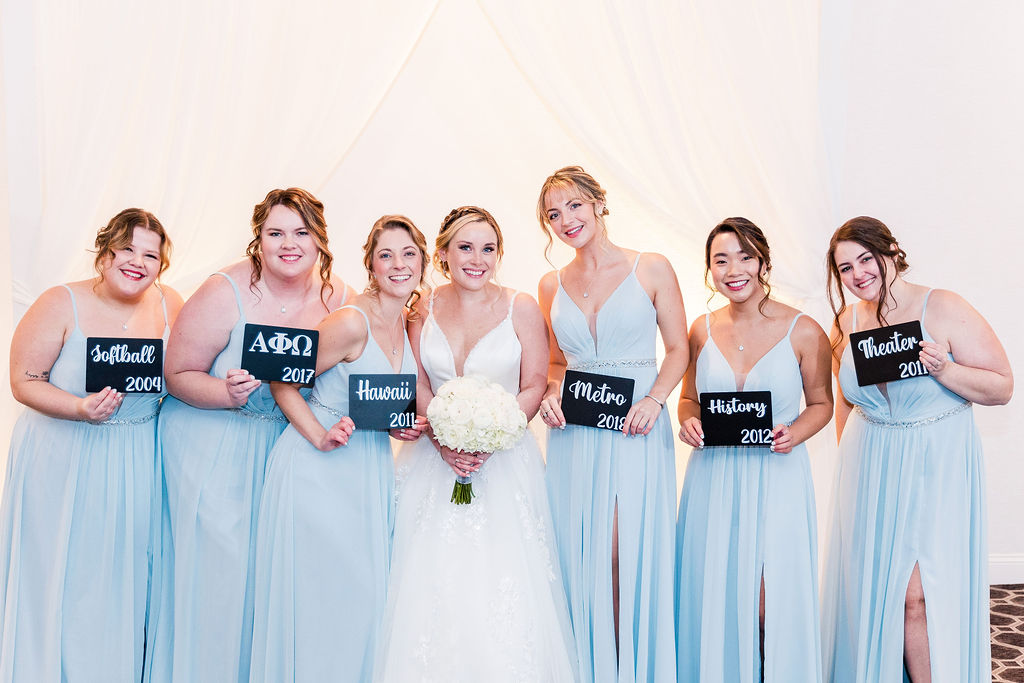 Wedding party pose with bridesmaids holding up signs of how they met the bride