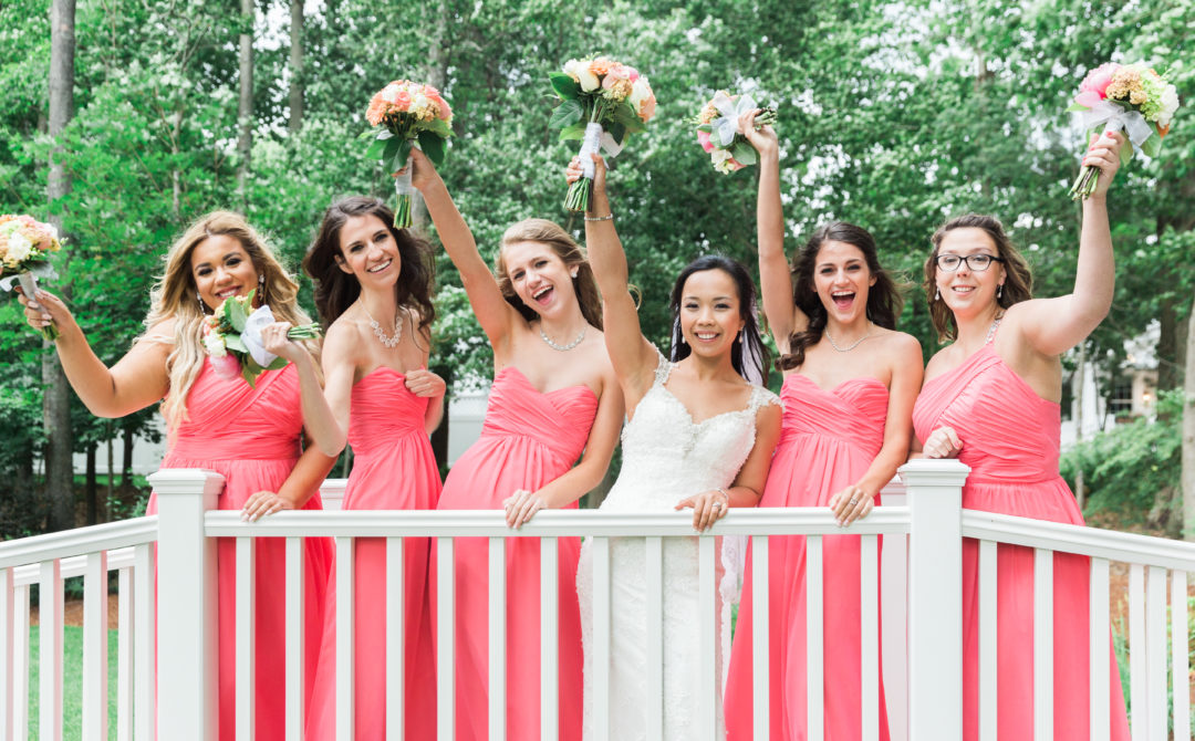 Bride and bridesmaids smiling on bridge in outdoor wedding ceremony
