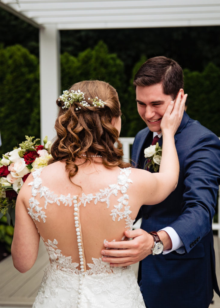 Groom reacts to bride as she walks down the aisle smiling in outdoor wedding ceremony at Saphire Estate in Sharon, Massachusetts