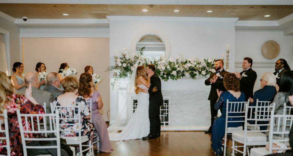 Bride and groom first kiss indoor wedding near beautiful fireplace inside Saphire Estate in Sharon, Massachusetts