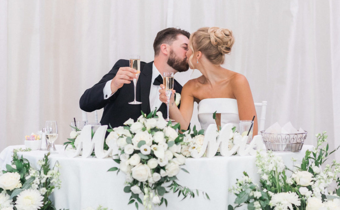 Couple Kissing and Holding Up Champagne at Sweetheart Table
