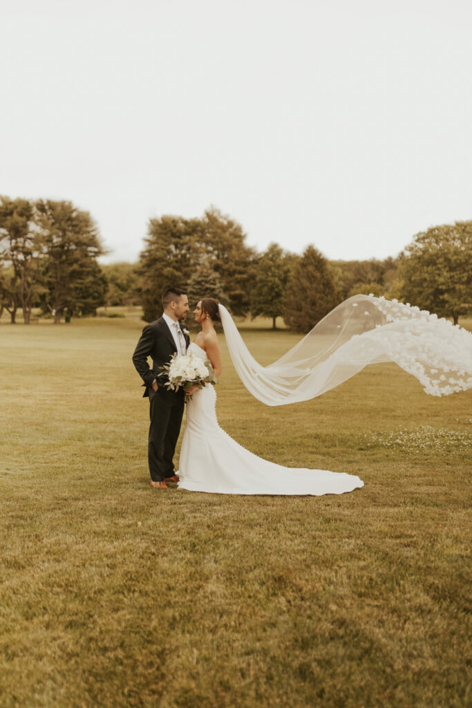 Bride and groom outside of The Villa in a field with veil blowing in the wind