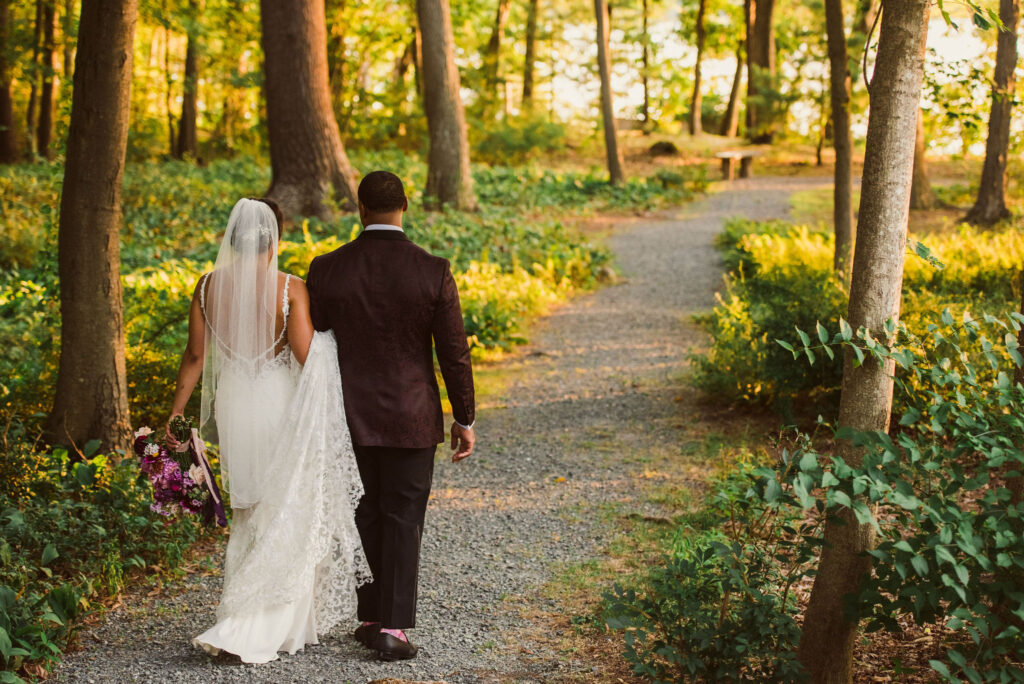 bride and groom walking down wooded path for wedding photo