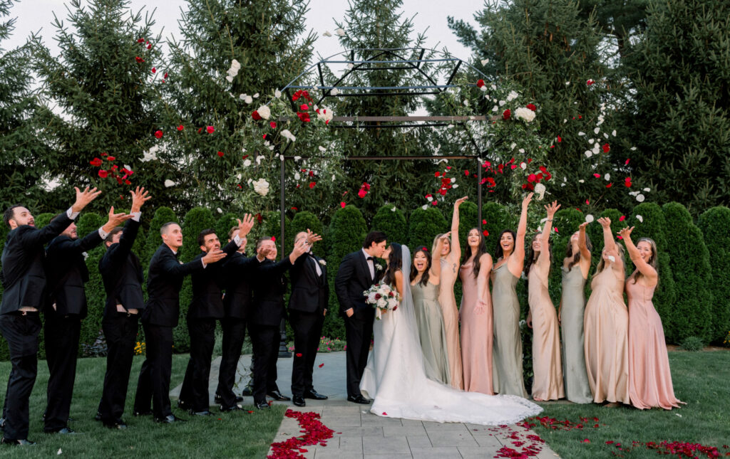 Wedding Party Throwing Rose Petals While Bride and Groom Kiss