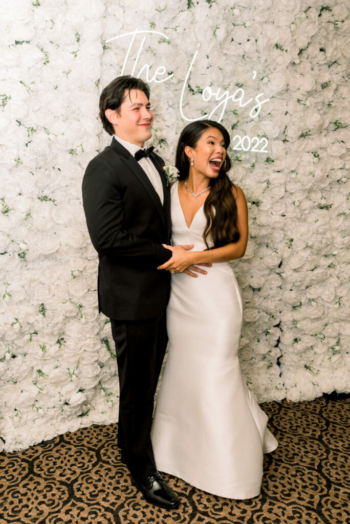 Bride and Groom Pose in front of White Rose Flower Wall at Massachusetts Wedding