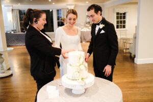 Wedding Producer Helps Bride and Groom Cut Cake at Saphire Estate Massachusetts Wedding