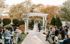 Bride and Groom Hold Hands at Fall Outdoor Wedding Ceremony at the Villa in East Bridgewater Massachusetts