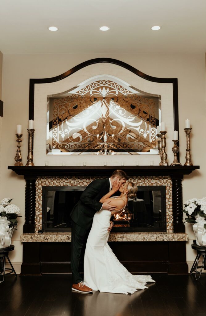 Bride and Groom Kiss in Front of Fireplace at The Villa at Ridder Country Club