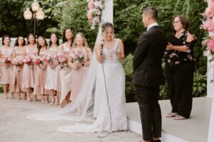 Bride Recites Vows While Bridesmaids in Pink Bridesmaids Dresses Watch and Smile