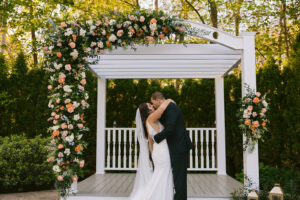 Bride and Groom First Kiss Under Florals and Pergola Fall Ceremony 