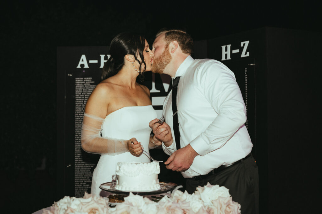 Bride and Groom Kiss Cake Cutting in Front of Seating Chart