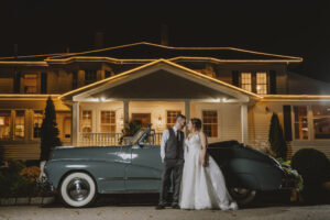 Bride and Groom Portrait With Vintage Car in Front of Historic Estate Lit up at Night