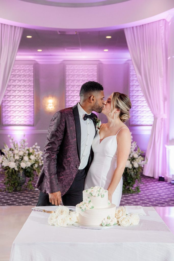 Bride and Groom Kissing Over Wedding Cake at Reception