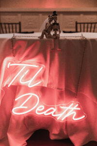 Red Neon Sign Reads Til Death With Bride and Groom Skeleton Figurines