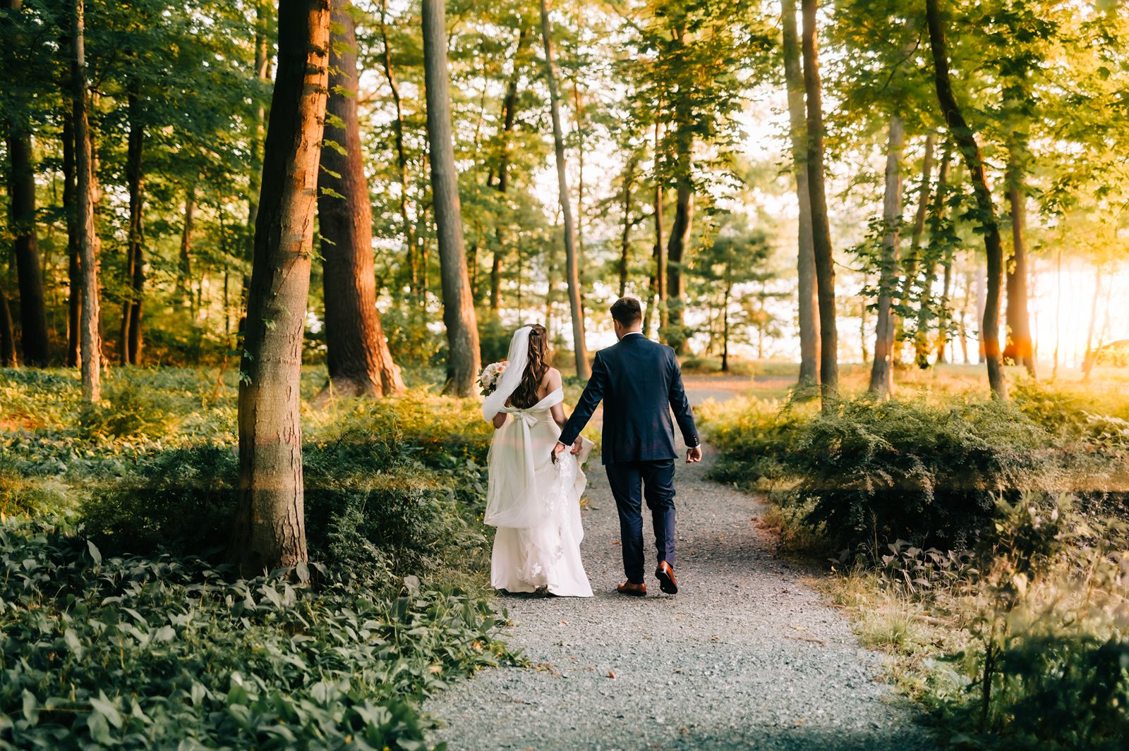 Bride and Groom Holding Hands Walking in Woods At Sunset 