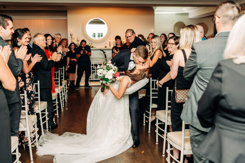 Bride and Groom Dip Kiss in Aisle Indoor Ceremony