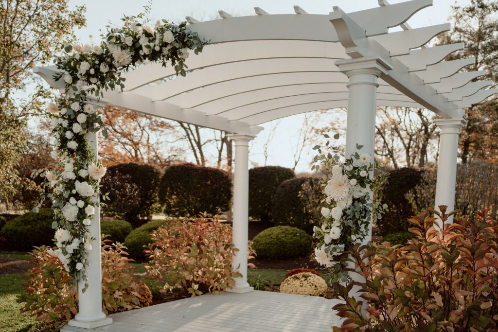 White pergola with cascading white florals in a fall garden.