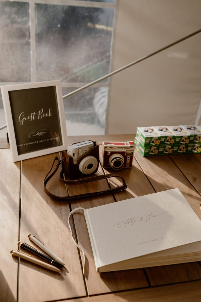 Guest book and instant camera on a table beside a sign.