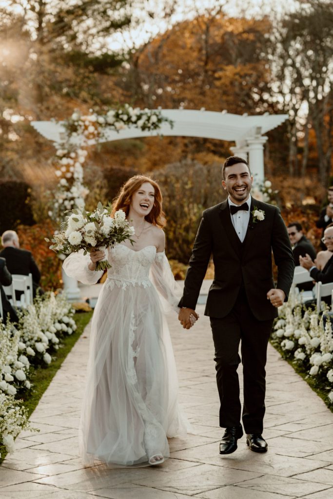 Bride and groom walking hand in hand up a flower-lined aisle.