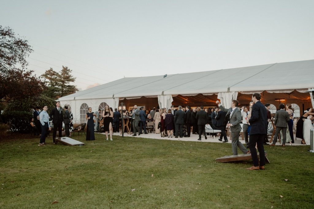 Guests gathered outside a white reception tent on a lawn at dusk.