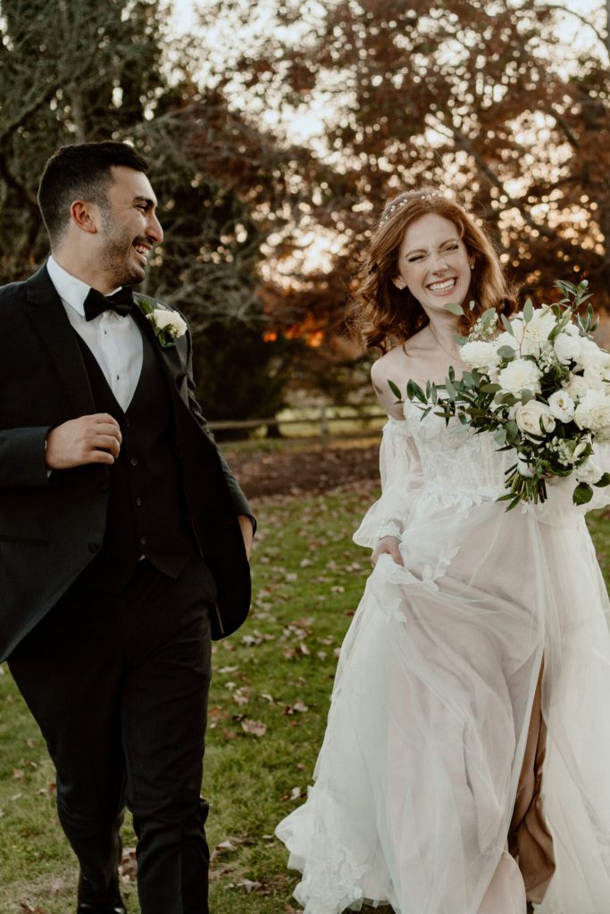 Bride and groom walking hand in hand across a lawn in the fall.