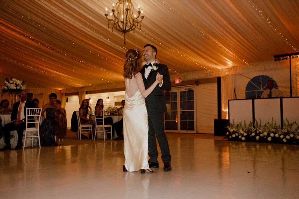 Bride and groom sharing a first dance in a tent with chandeliers.
