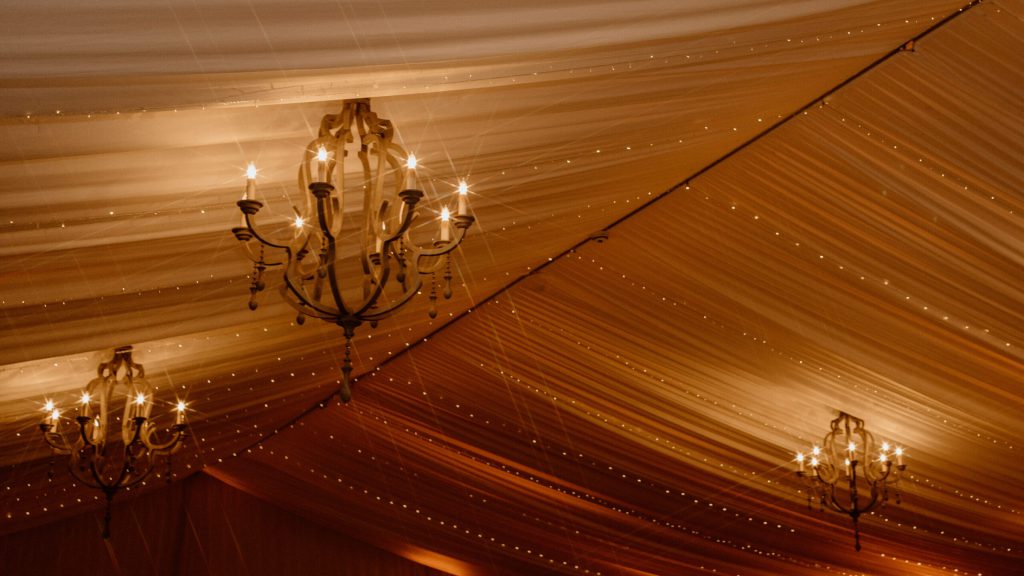 Draped tent ceiling with chandeliers and warm string lights.