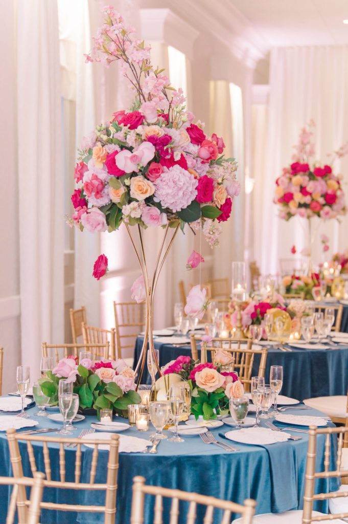 Reception tables with navy linens, gold chairs and tall pink floral centerpieces.