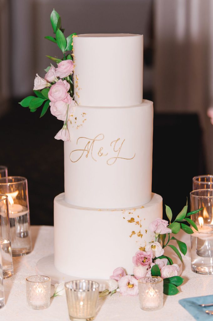 Three-tier white wedding cake with a monogram and pink florals.