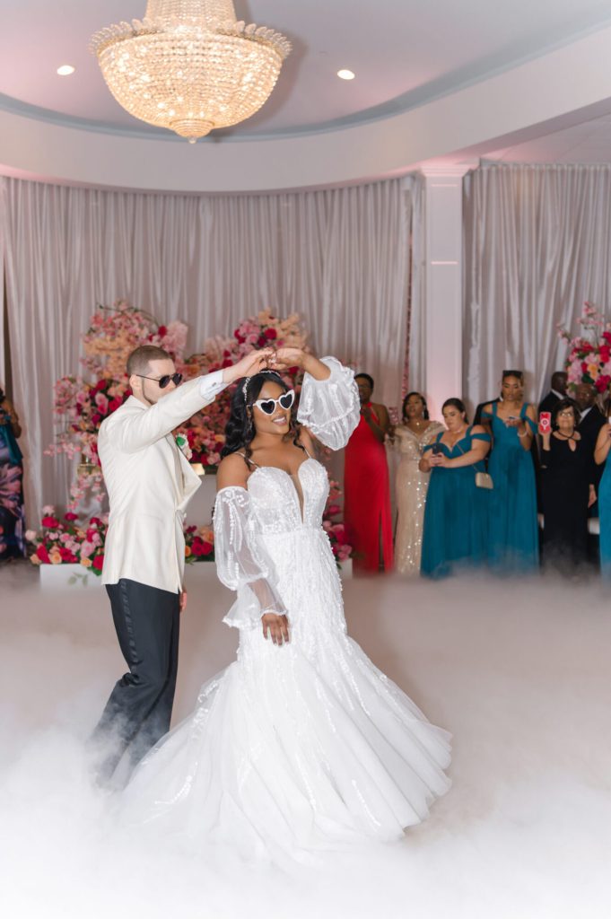 Bride and groom dancing on a fog-covered dance floor beneath a chandelier.