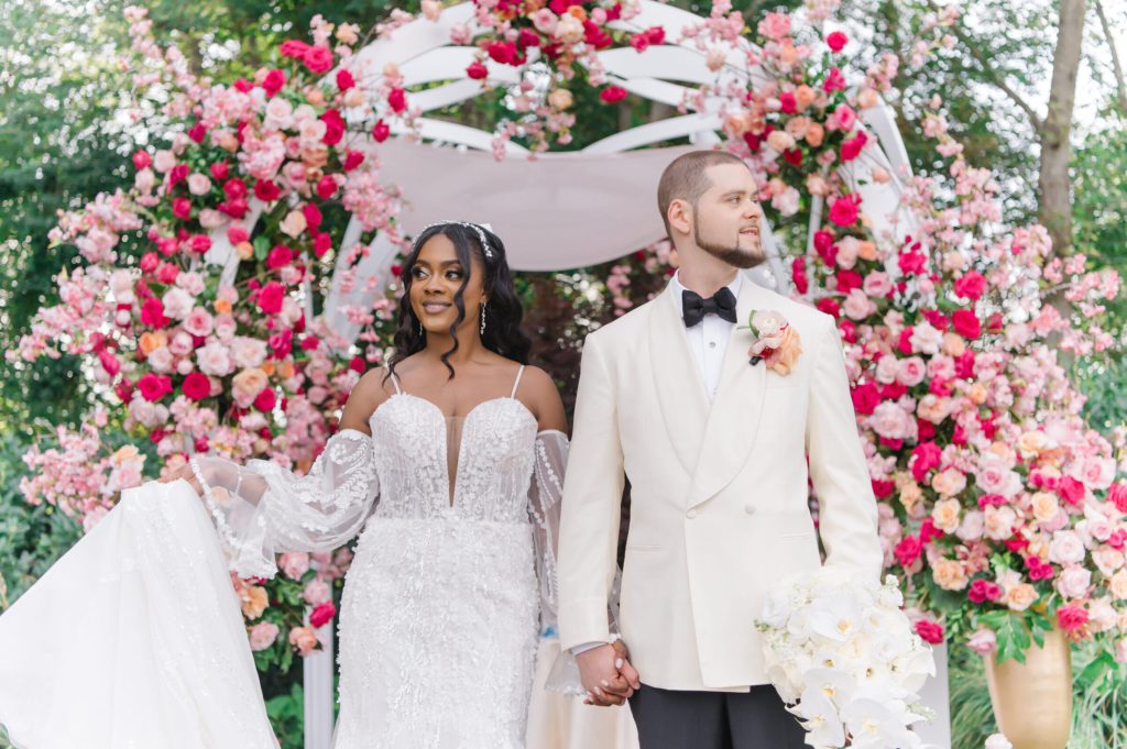Bride and groom smiling beneath a pink floral arch.