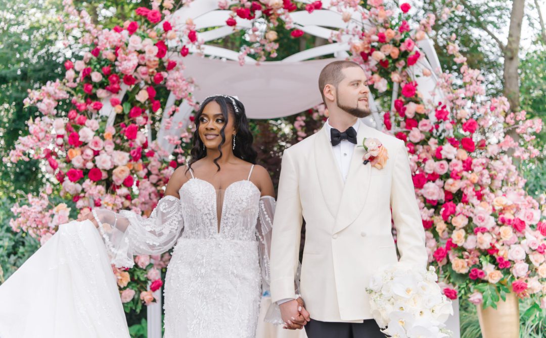 Bride and groom smiling beneath a pink floral arch.