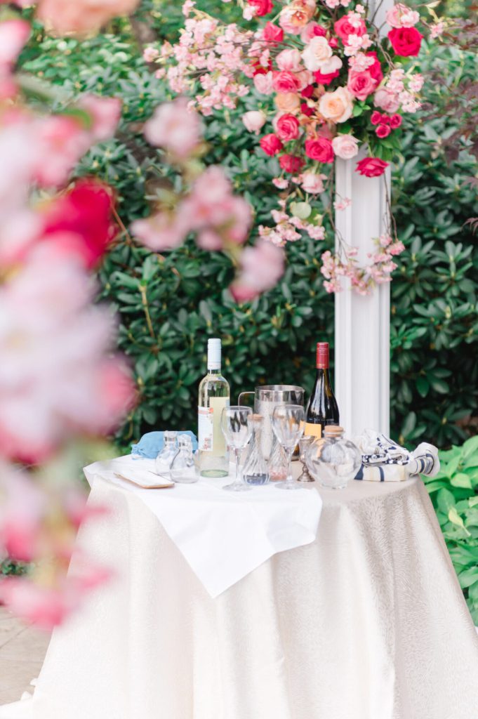 Round table with white linens beside a pink floral installation.