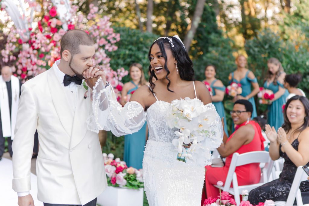 Groom kissing the bride's hand as they recess from a garden ceremony.