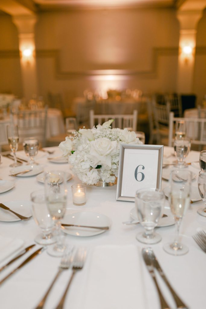 Round reception table with white florals and a table number in warm light.