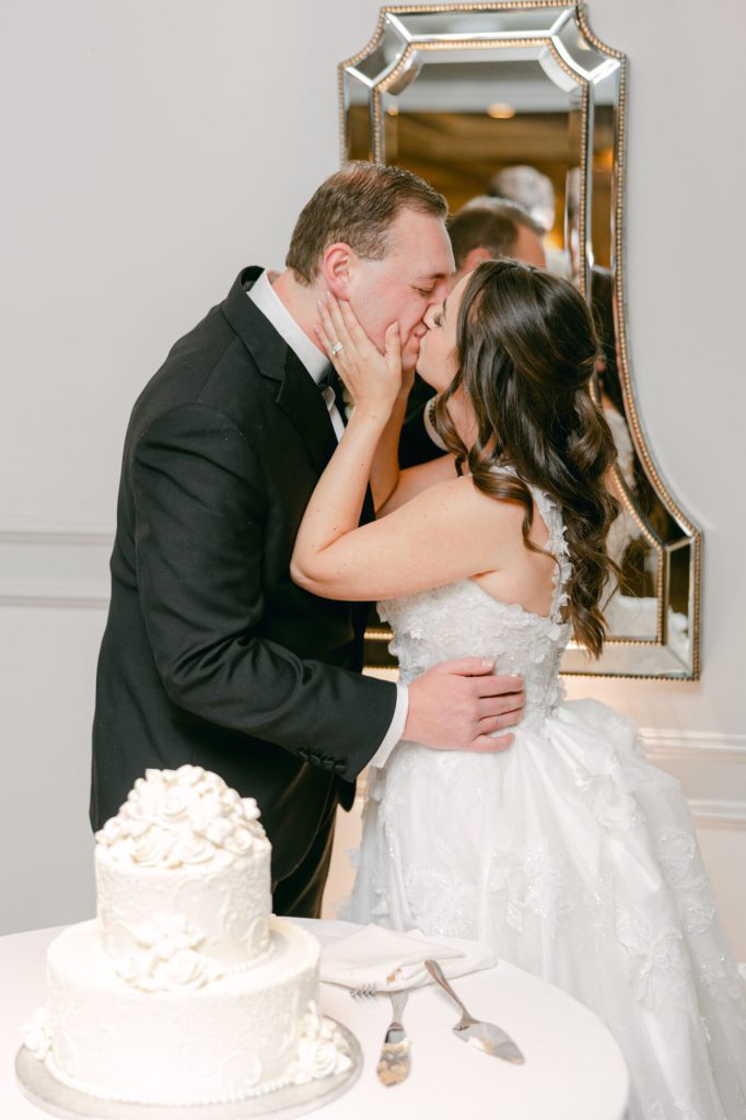Bride and groom kissing beside their wedding cake.